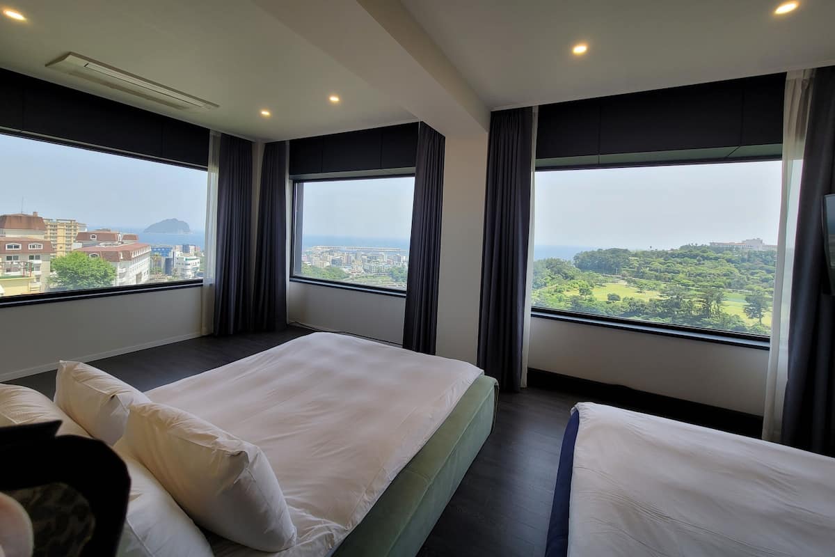 A hotel room with two beds, large windows, and a city view.