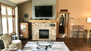 Un salon avec une cheminée en pierre, un téléviseur à écran plat, une table basse en verre et un canapé.
