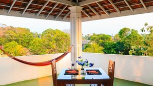 A balcony with a table set for two, a hammock, and a view of greenery. - Hotel Nathariya Negombo (Negombo)