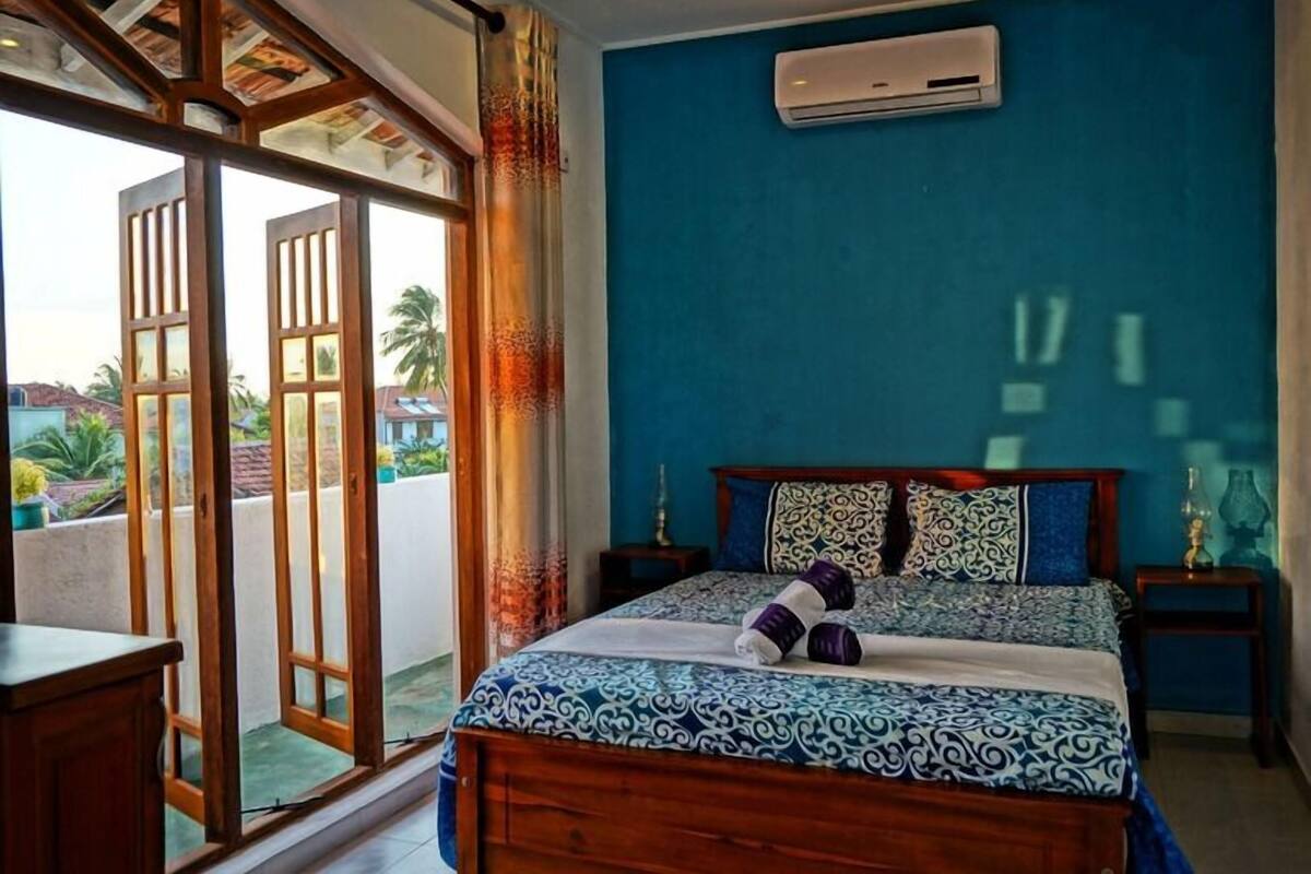A bedroom with a bed, a nightstand, a lamp, and a view of the outside.