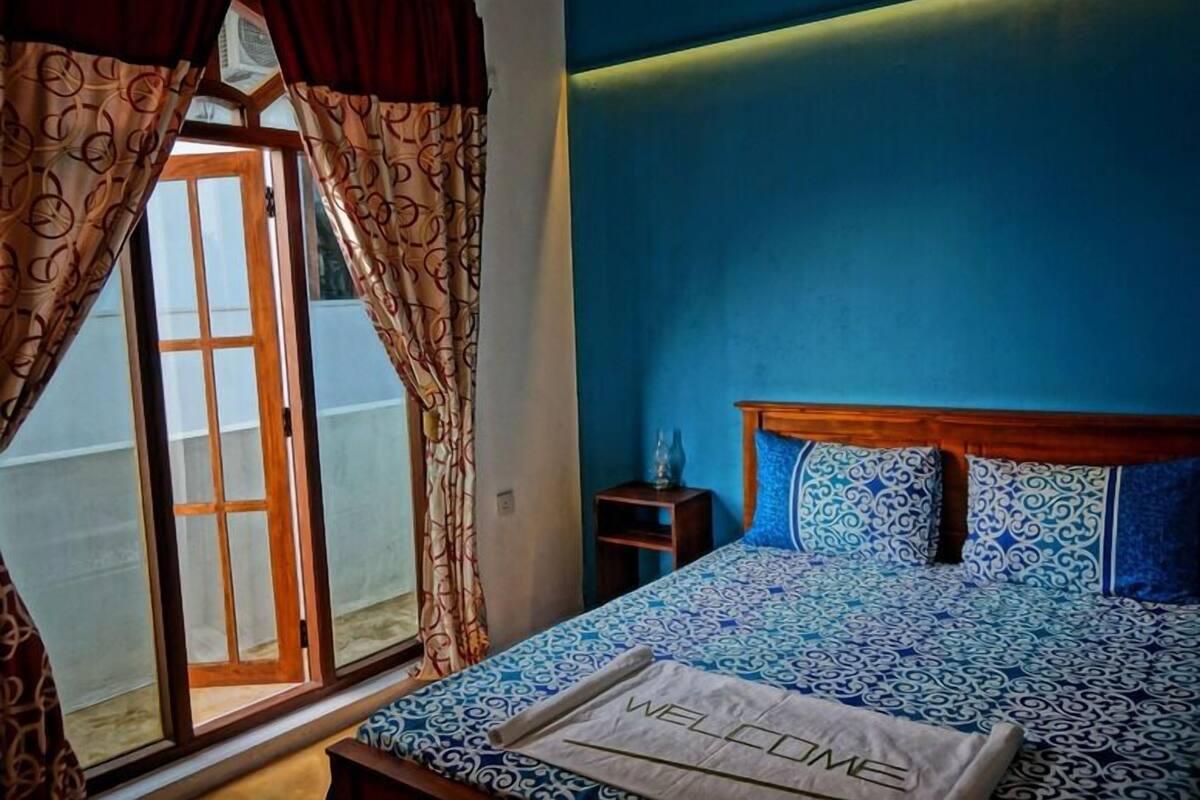 A bedroom with a bed, curtains, a window, and a welcome mat.