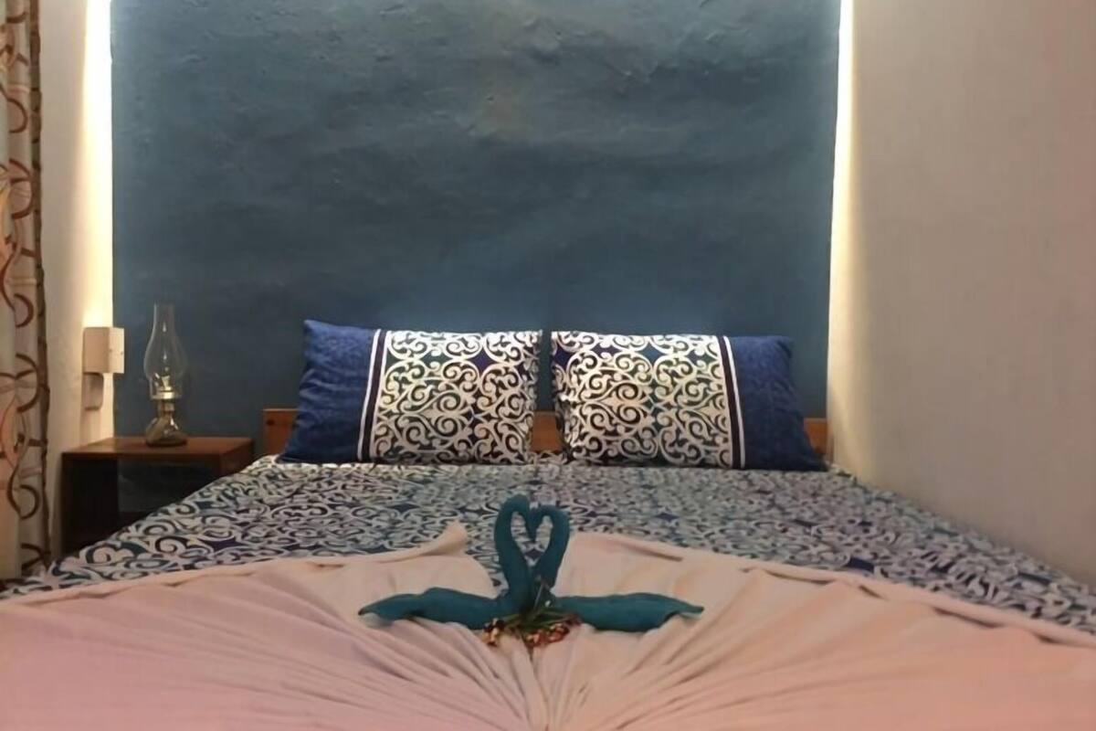 A bed with a patterned bedspread, two pillows with a blue and white design, and a decorative item in the center.