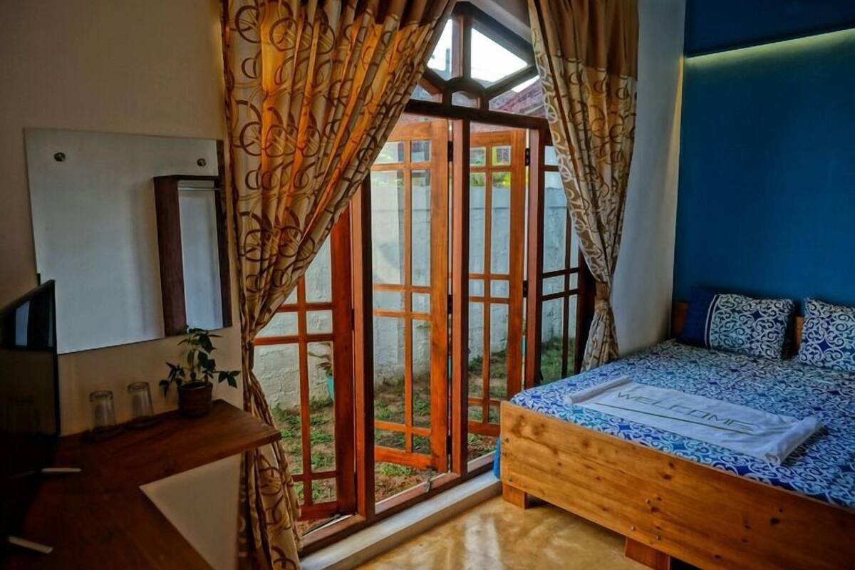 A bedroom with a bed, a wooden nightstand, a TV, and a window with curtains.