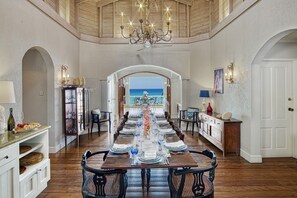 A dining room with a long table set for a meal, a chandelier, and a view of the ocean. - La Paloma by Blue Sky Luxury (Prospect)