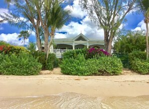 A beachfront property with a white building featuring a covered patio area, surrounded by lush greenery and palm trees. - La Paloma by Blue Sky Luxury (Prospect)