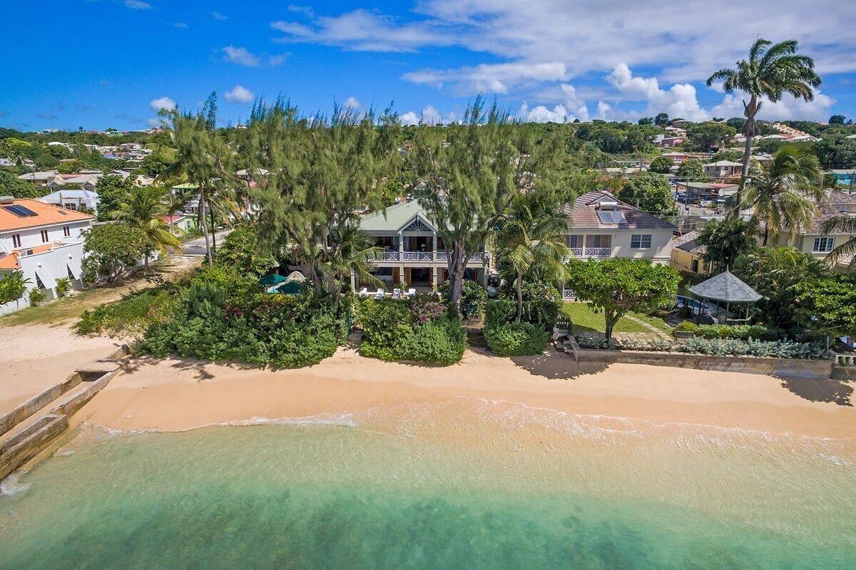Um imóvel à beira-mar com uma casa grande, piscina e vegetação exuberante.