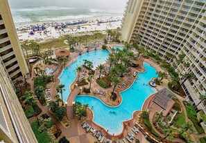 Un hotel con una piscina ampia e dalla forma irregolare, circondata da palme e sdraio. Si intravede una spiaggia sullo sfondo.