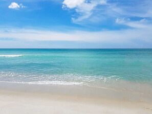 Ein Strand mit klarem türkisblauem Wasser und einem sandigen Ufer unter blauem Himmel.