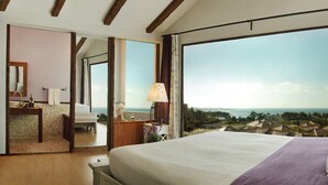 A bedroom with a large bed, a nightstand, a lamp, and a view of the ocean. - Olle Resort & Spa (Jeju City)