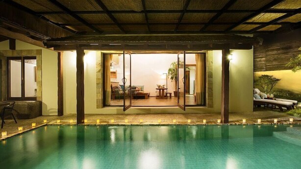 A swimming pool with a glass enclosure, a thatched roof, and a view into a room with a sofa and a table. - Olle Resort & Spa (Jeju City)