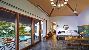 A spacious room with a large sliding glass door leading to an outdoor pool area, a wooden dining table with chairs, and a cozy seating area with a sofa and a coffee table. - Olle Resort & Spa (Jeju City)