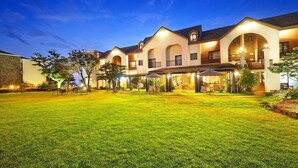 A multi-story hotel with a well-lit outdoor area, including a covered patio and a grassy lawn. - Olle Resort & Spa (Jeju City)