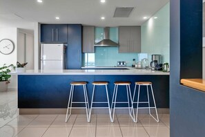 A modern kitchen with a central island, bar stools, and a stainless steel refrigerator.