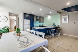 A modern kitchen with a central island, white bar stools, and a dining table with a woven placemat.