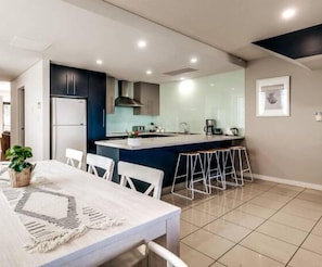 A modern kitchen with a central island, bar stools, and a dining area with a table and chairs.