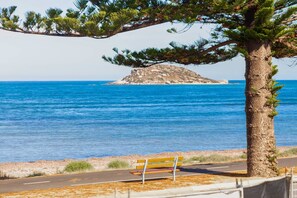 A bench by the roadside with a view of the sea and a rocky island in the distance.