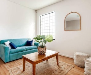 A living room with a teal sofa, a wooden coffee table, a potted plant, a woven rug, and a mirror on the wall.