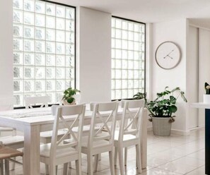 A bright, modern kitchen with white cabinetry, a large window with a grid pattern, and a round wall clock.