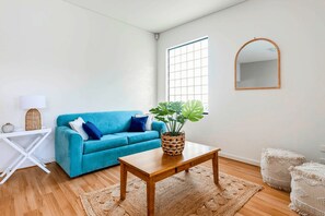 A living room with a blue sofa, a wooden coffee table, a potted plant, a white lamp, and a mirror on the wall.