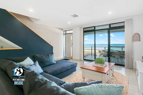 A modern living room with a dark blue sofa, a wooden coffee table with a plant, and a view of the ocean through large glass doors.