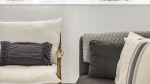 Een kamer met een raam, een stoel, een bank en twee gevlochten lampen.