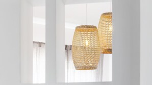 Een witte ruimte met een tafel en stoelen, en twee hangende rieten lampen.