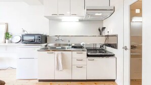 A modern kitchen with white cabinets, a microwave, a stove, and a sink. - Commence5 (Sapporo)
