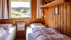 Una habitación de cabaña de madera con dos camas, una ventana con vistas, un calentador fijado a la pared y una repisa con frascos.