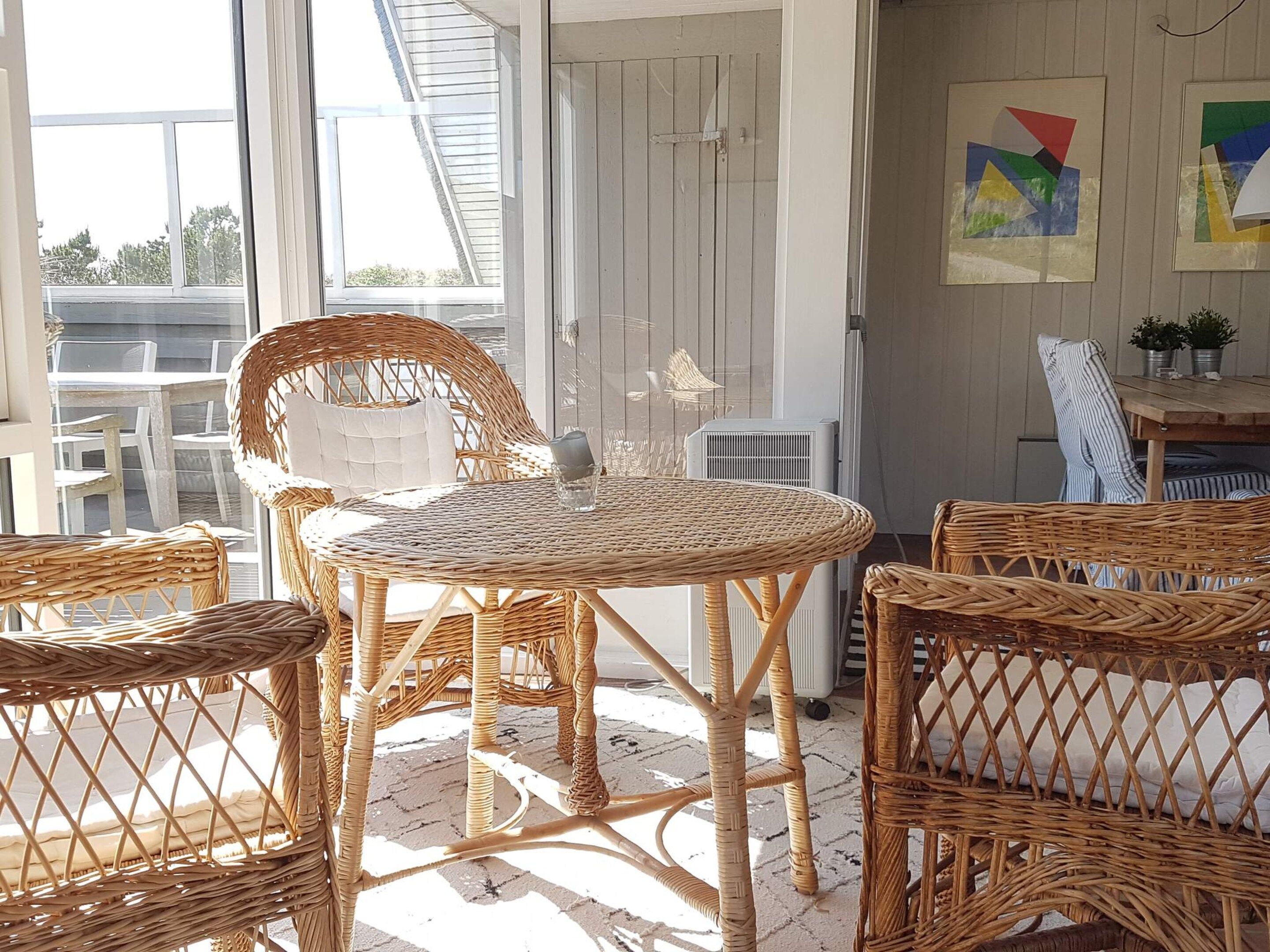A wicker table and chairs on a balcony with a view of the sky and trees.