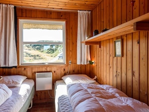 A cabin with two beds, a window with a view, and a shelf with items.