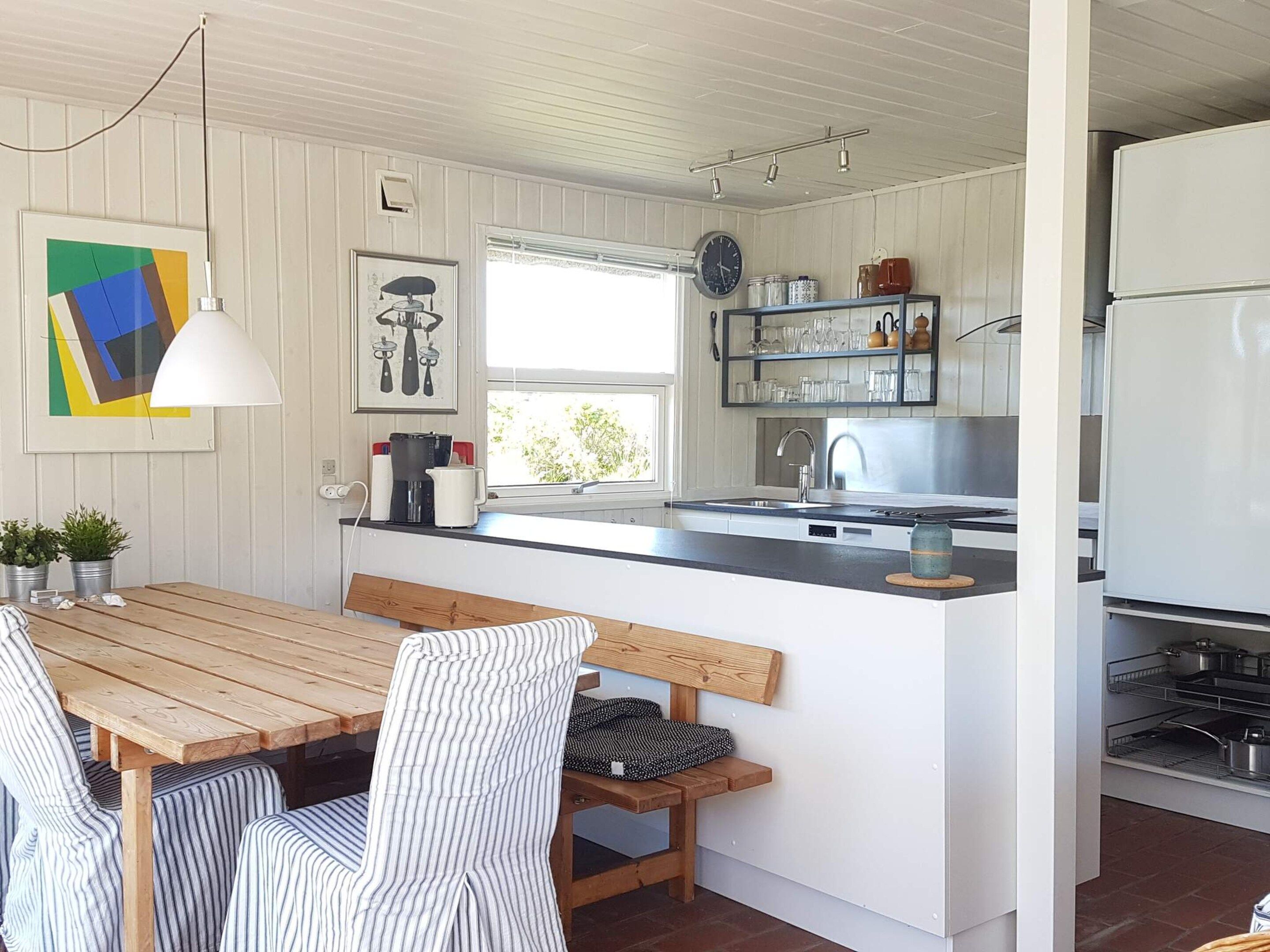 A kitchen with a wooden table, striped chairs, a bench, a sink, and a refrigerator.