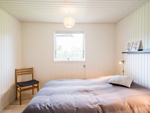 A bedroom with a bed, a chair, a window, and a shelf with pictures.