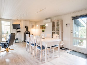 A dining area with a white table, wooden chairs, a black chair, a fireplace, a television, and a door with a view to the outside.