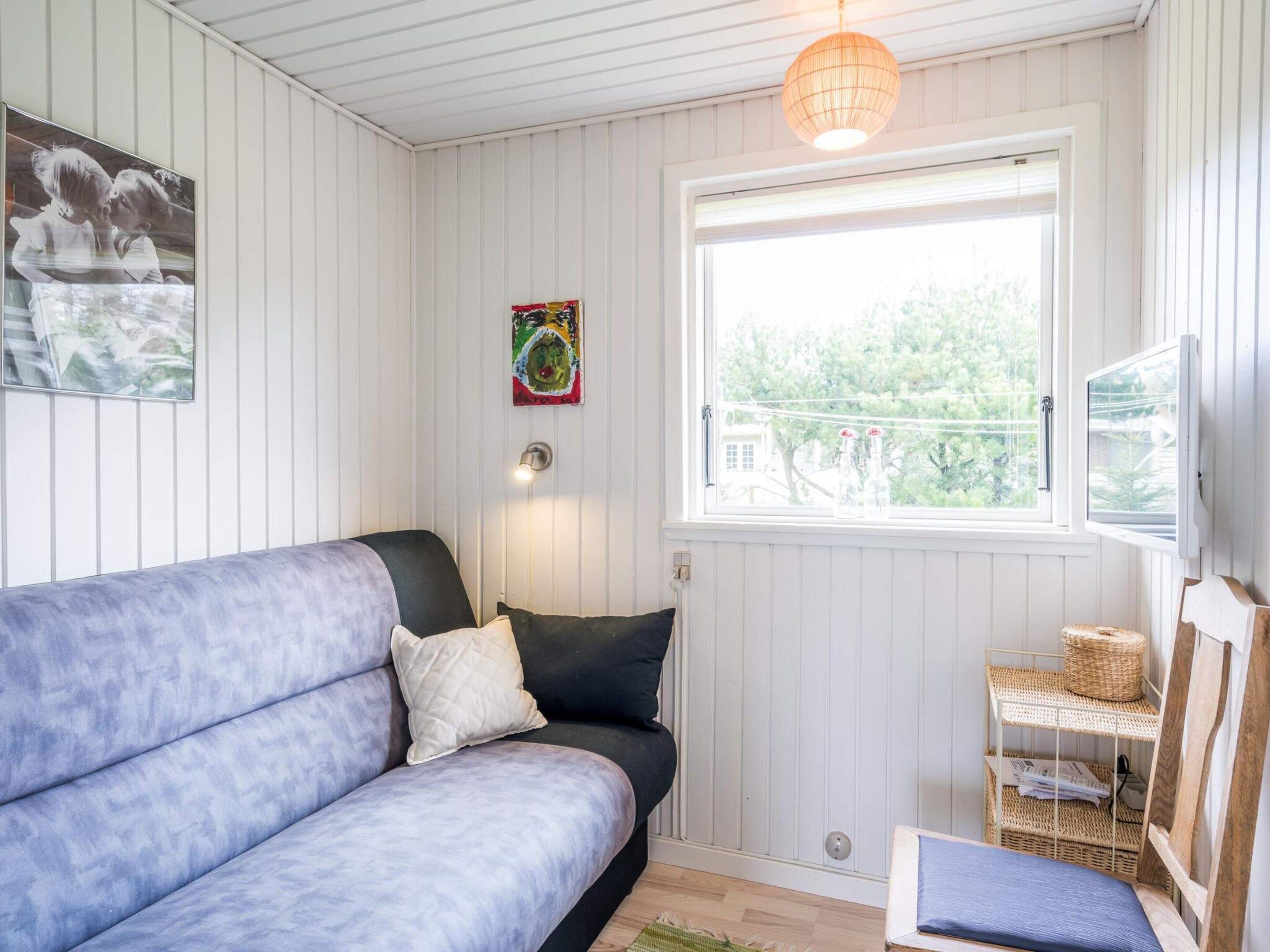 A room with a sofa, a window with a view, a wall-mounted light, and a shelf with baskets.