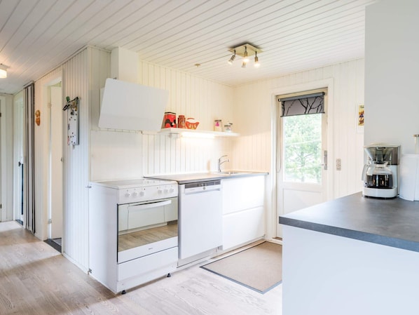 A compact kitchen with white cabinetry, a built-in oven, a dishwasher, and a coffee maker.