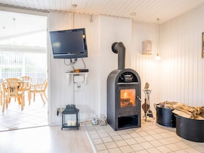 A room with a fireplace, a television mounted on the wall, wicker chairs, and a tiled floor.