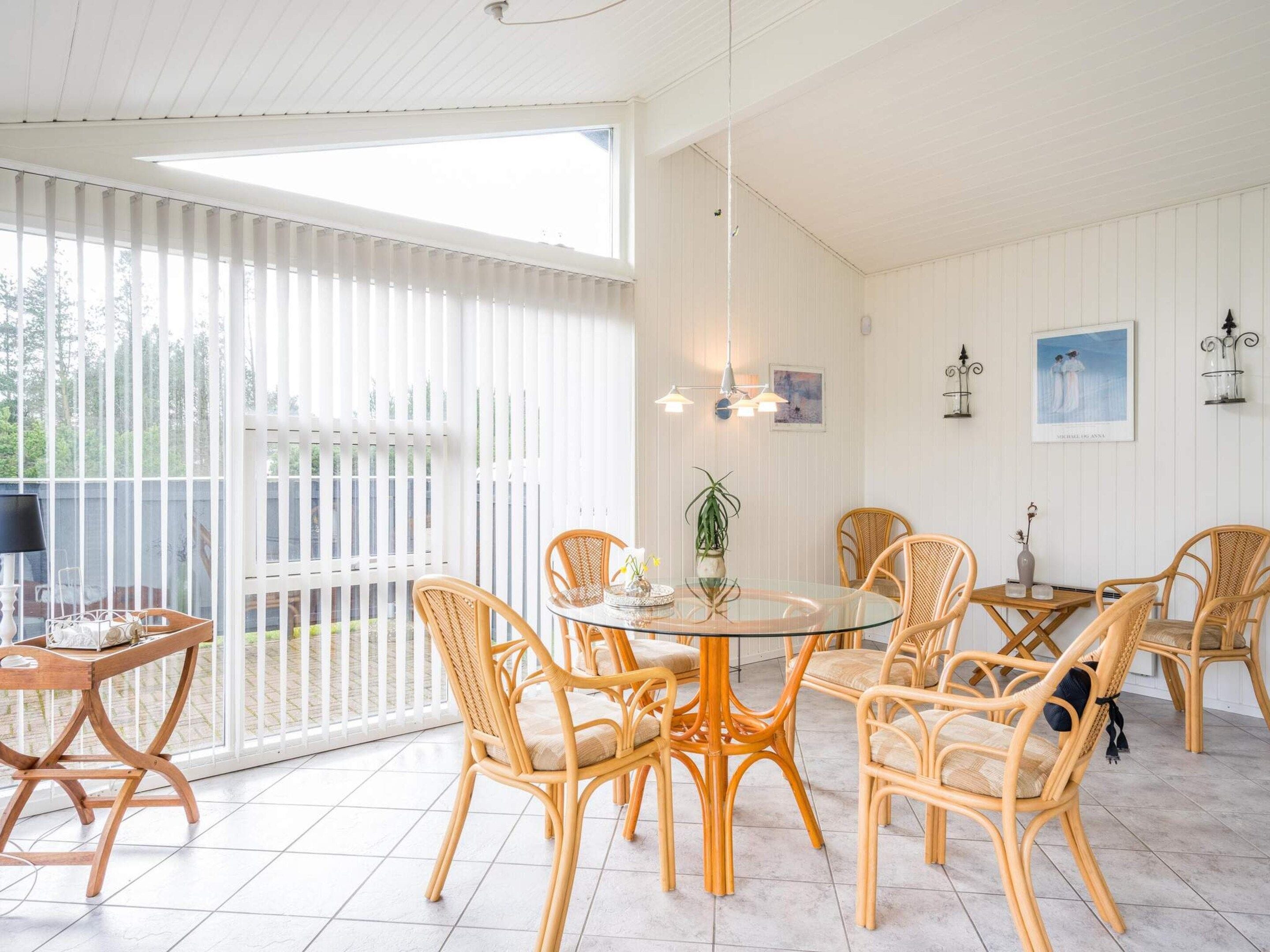 A dining area with wicker chairs, a round glass table, and a white ceiling.