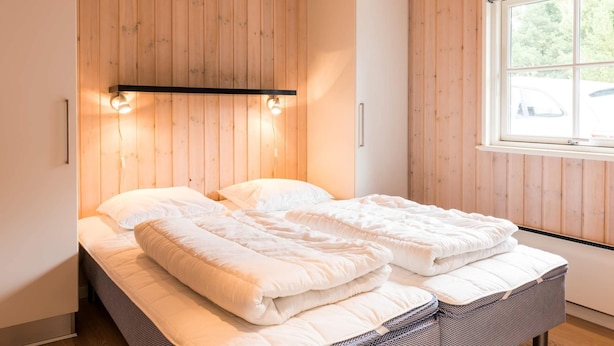 Une chambre à coucher avec un lit, des murs en bois, une fenêtre et une étagère avec des lampes.