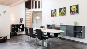 A modern kitchen with a dining area, featuring a round table, black chairs, and a grey cabinet. - 5 Star Holiday Home in Blavand (Blavand)