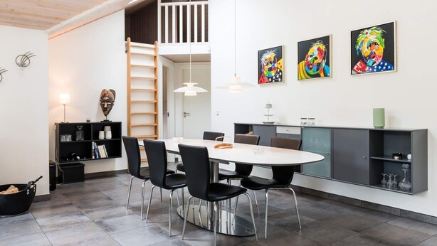 A modern kitchen with a dining area, featuring a round table, black chairs, and a grey cabinet. - 5 Star Holiday Home in Blavand (Blavand)