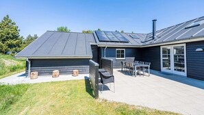 A modern house with a covered patio, a chimney, and a large window. - 5 Star Holiday Home in Blavand (Blavand)