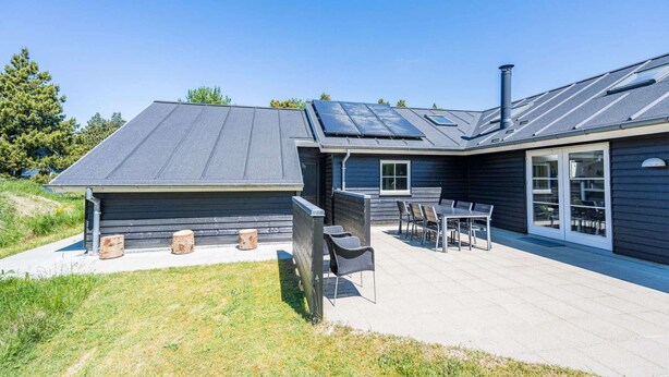 A modern house with a covered patio, a chimney, and a large window. - 5 Star Holiday Home in Blavand (Blavand)