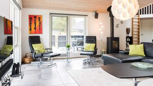 A modern living room with a fireplace, two black leather sofas with green cushions, a black coffee table, and a large window with a view of the outside. - 5 Star Holiday Home in Blavand (Blavand)