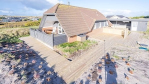 A coastal house with a sloped roof, a wooden deck, and a sandy beach in the foreground. - 6 Person Holiday Home in Hvide Sande (Hvide Sande)