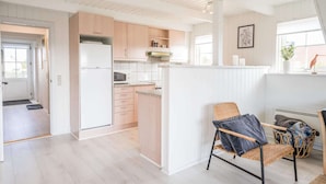 A modern kitchen with wooden cabinets, a white refrigerator, and a microwave. There is a wicker chair and a basket with items on the floor. - 6 Person Holiday Home in Hvide Sande (Hvide Sande)