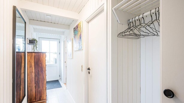 A hallway with white walls, a wooden door, and a metal rack with hangers. - 6 Person Holiday Home in Hvide Sande (Hvide Sande)