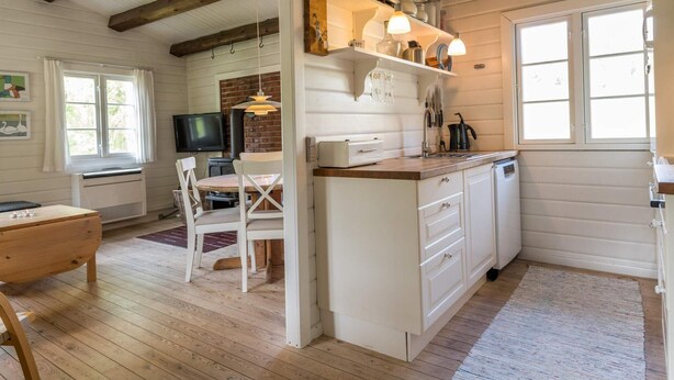 A kitchen with wooden beams, white cabinets, a dining area with a table and chairs, and a fireplace.