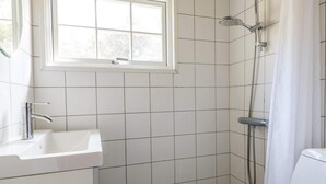 A bathroom with white tiles, a window, a sink, and a shower.