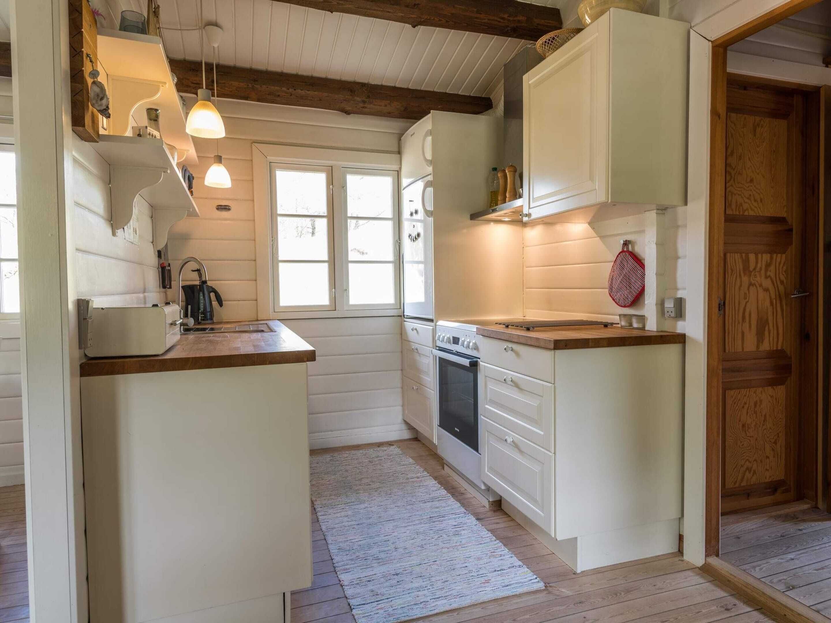 A kitchen with white cabinetry, a wooden countertop, and a built-in oven. There are pendant lights above the sink and a window providing natural light.