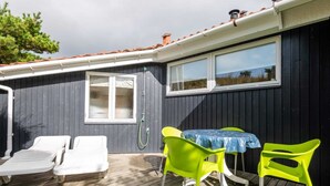 Eine Terrasse mit zwei weißen Liegestühlen, einem Tisch mit blauer Tischdecke und zwei hellgrünen Stühlen.